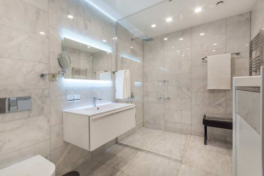 Ванная комната с душем из каррарского мрамора, косметическим зеркалом, плавающей столешницей, держателем для полотенец и потолочными светильниками.
