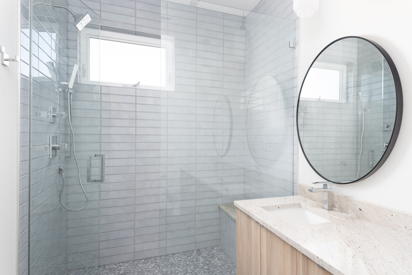 Ванная комната со стеной, выложенной плиткой из каррарского мрамора, душем, столешницей, зеркалом и туалетным столиком.