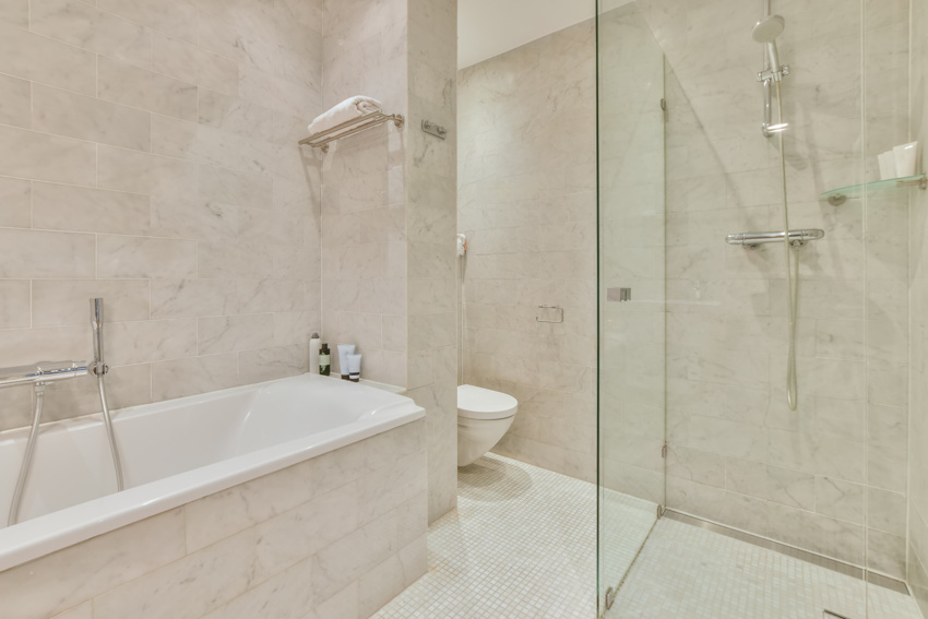 Ванная комната со стеклянной перегородкой, ванной, душевой зоной, стеной из каррарского мрамора и кафельным полом.