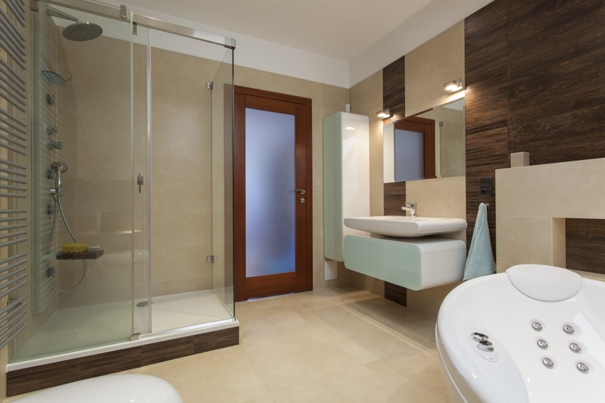Ванная комната из известняка с душевой кабиной, стеклянной дверью, парящим туалетным столиком и зеркалом.