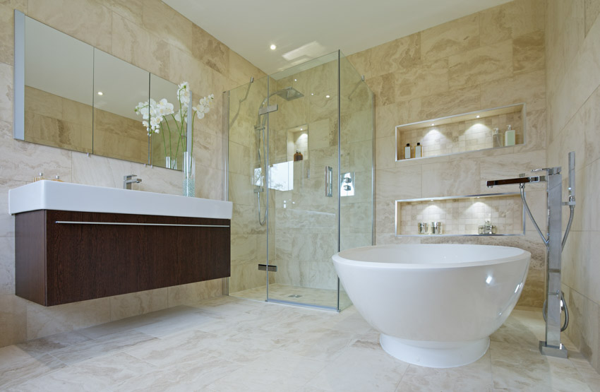 Ванная комната с известняковым душем, полом, стеклянной ванной, дверью, плавающей раковиной и зеркалом.