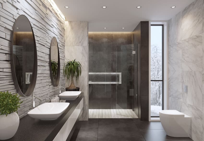 Современная минималистская ванная комната с большой черной плиткой, гранитной столешницей, зеркалами, туалетом, комнатными растениями и душевой.