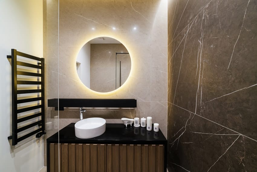 Ванная комната с черной столешницей, зеркалом с подсветкой, держателем для полотенец, раковиной, краном и акцентной стеной