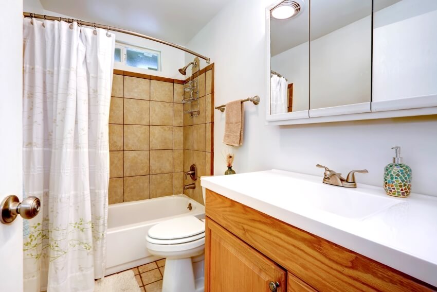 Интерьер ванной комнаты с отделкой стен плиткой, изогнутой латунной штангой для душа и деревянным туалетным столиком