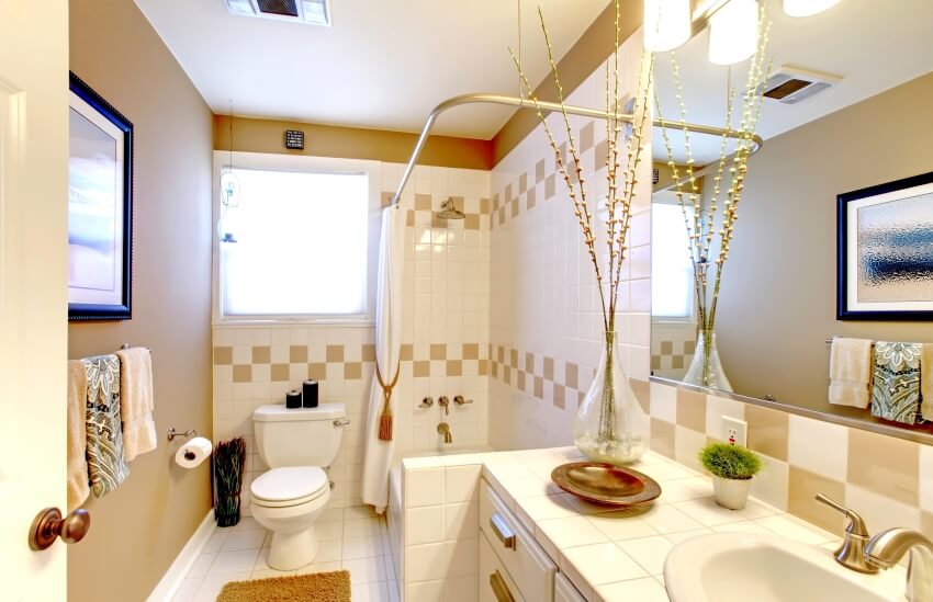 Ванная комната в светлых тонах с отделкой стен плиткой и столешницей из плитки, а также угловой штангой для душа с занавеской