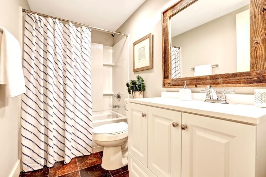 Ванная комната в белых тонах с туалетным столиком, зеркалом в деревянной раме и полосатой занавеской для душа