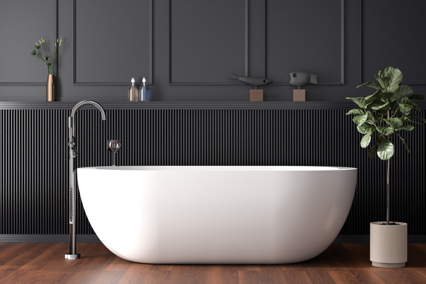 Ванная комната с отдельно стоящим краном в белой ванне, деревянным полом, обшивкой стен и комнатным растением