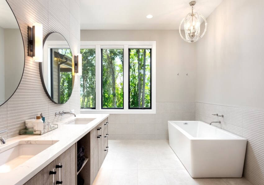 Элегантная ванная комната с двумя раковинами, отдельно стоящей ванной, окнами и столешницей из кварцита.