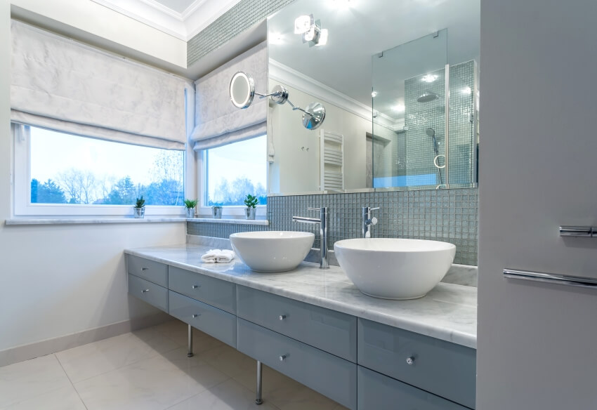 Современная ванная комната с двумя раковинами на столешнице из кварцита, фартуком из стеклянной плитки и окнами.