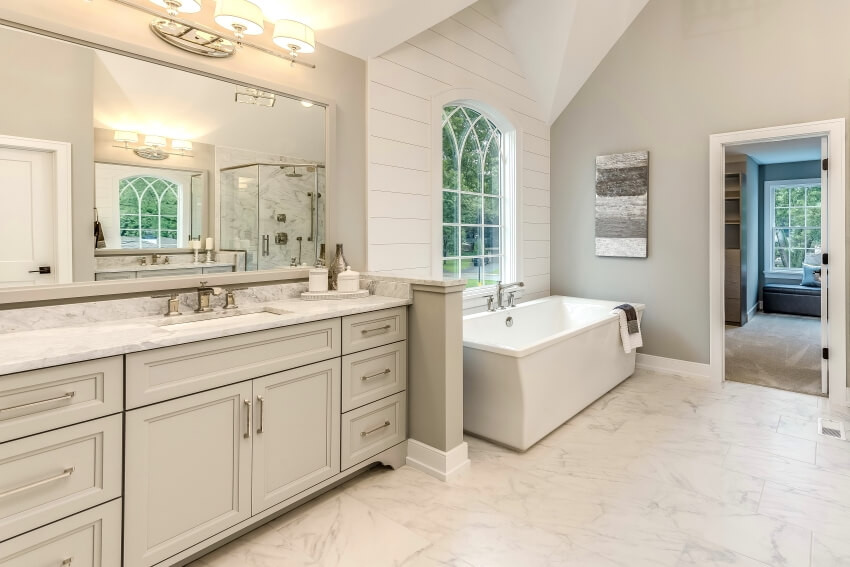 Мраморная ванная комната с отдельно стоящей ванной, стильным освещением и встроенной раковиной в туалетном столике.