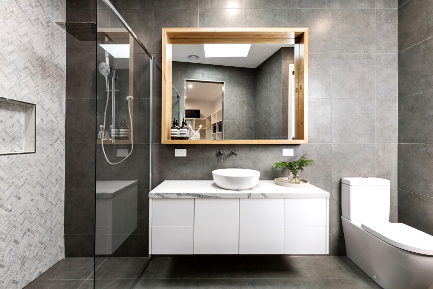 Современная серая ванная комната с плиткой для душа в елочку и парящим туалетным столиком с зеркалом в деревянной раме.