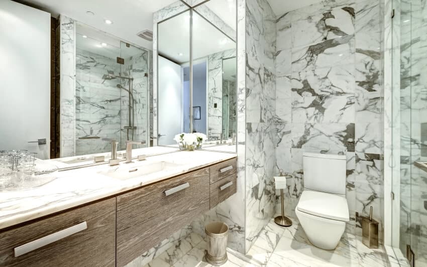 Ванная комната с мраморной плиткой на стене и полу, большим зеркалом и мраморной столешницей.