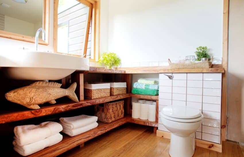 Современный интерьер ванной комнаты с туалетом у кафельной стены и туалетными принадлежностями на деревянных полках