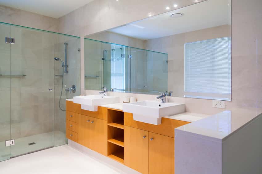 Ванная комната с душевой зоной, стеклянная дверь, шкафчики из медового дуба, раковины, зеркало и смесители.