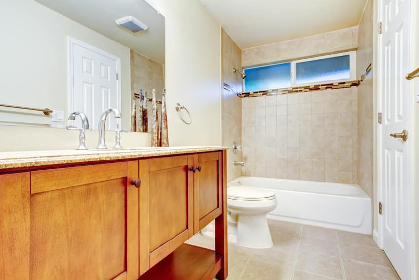 Ванная комната с косметическим зеркалом, шкафами из медового дуба, ванной, туалетом, окном и насадкой для душа.