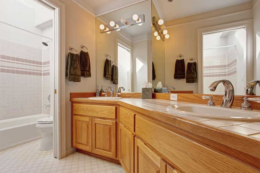 Туалетный столик в ванной комнате со шкафчиками из медового дуба, столешницей из плитки, раковиной, смесителем и зеркалом