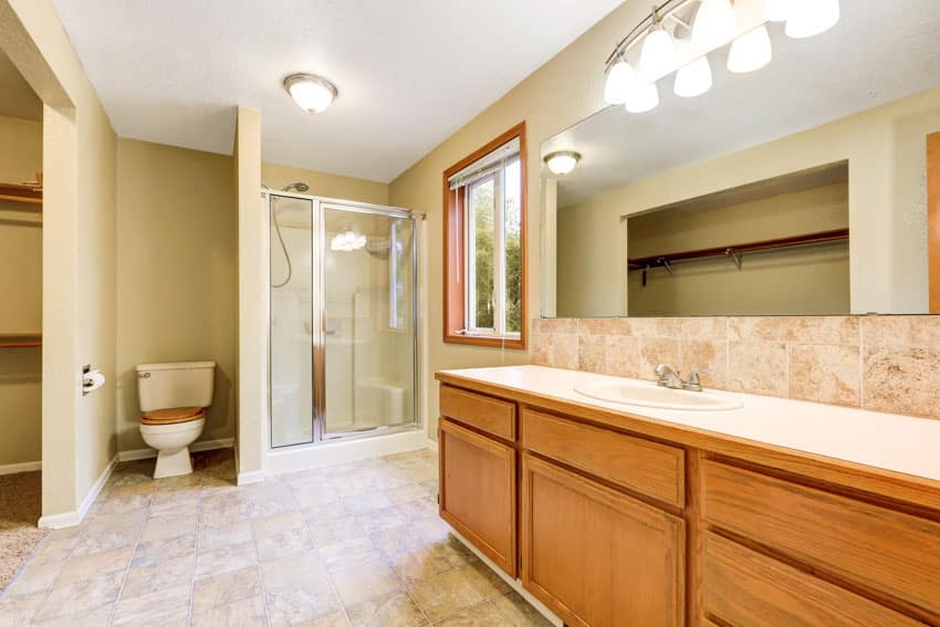 Ванная комната со шкафчиком из медового дуба, косметическим зеркалом, столешницей, душевой, туалетом и окнами.