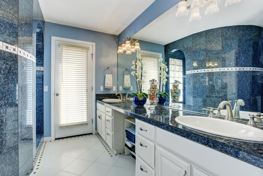 Ванная комната со столешницей из синего гранита, белыми ящиками, кафельным полом, зеркалом и стеклянной дверью.