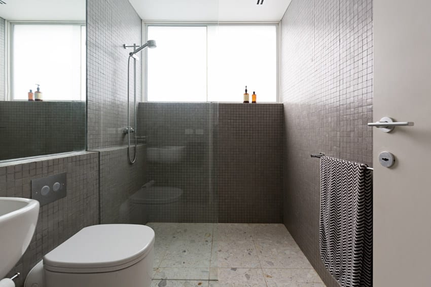 Ванная комната с полом из терраццо, стеклянной перегородкой, душем, окном, туалетом и зеркалом.