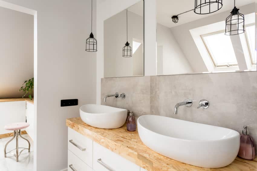 Ванная комната с деревянной столешницей, зеркалом, раковинами, смесителями и подвесными светильниками.