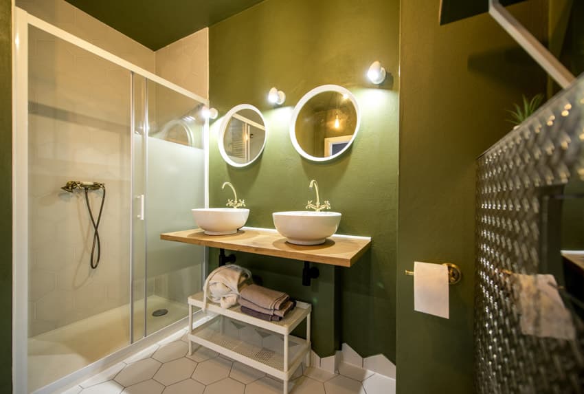 Ванная комната с зеленой стеной, парящим туалетным столиком, стеклянной дверью, раковинами, зеркалами и душевой кабиной.