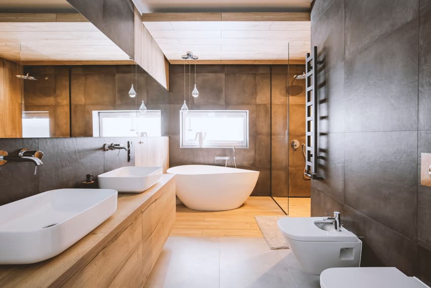 Современная ванная комната с туалетным столиком, деревянным полом, ванной, зеркалом, раковиной и туалетом.
