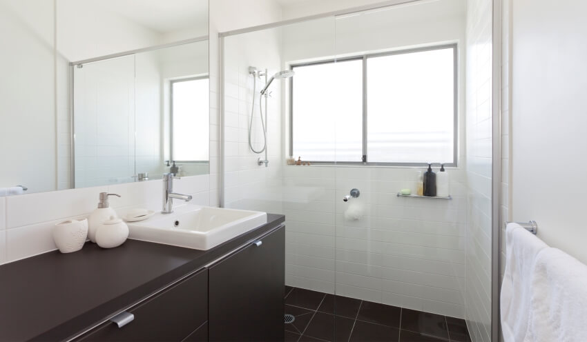 Современная ванная комната с белыми стенами, полом из черной плитки и столешницей, окрашенной в темный цвет.