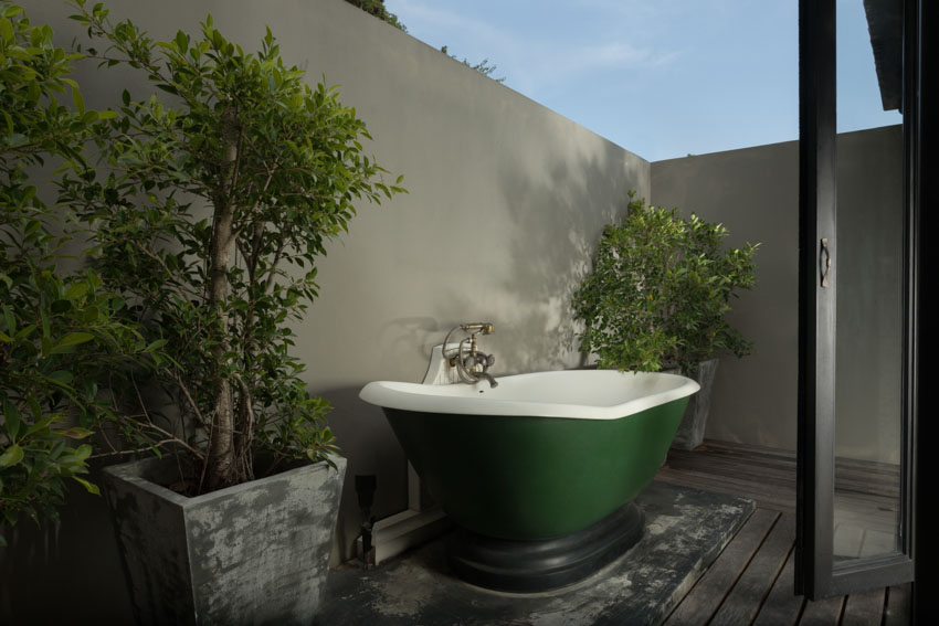 Уединенная ванна на открытом воздухе с зеленой ванной, деревянным полом и растениями