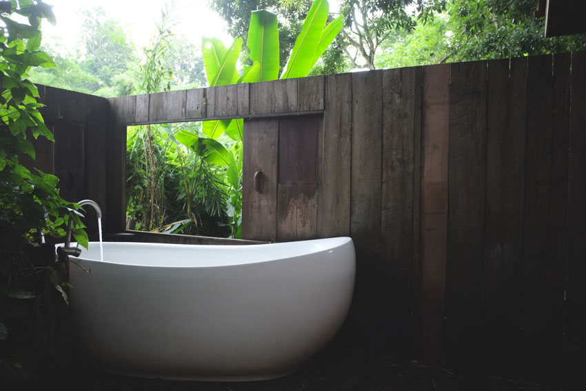 Ванна на открытом воздухе с белой ванной, деревянным забором и растениями
