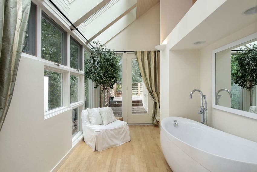Современная ванная комната с деревянными полами, большими окнами и креслом для отдыха