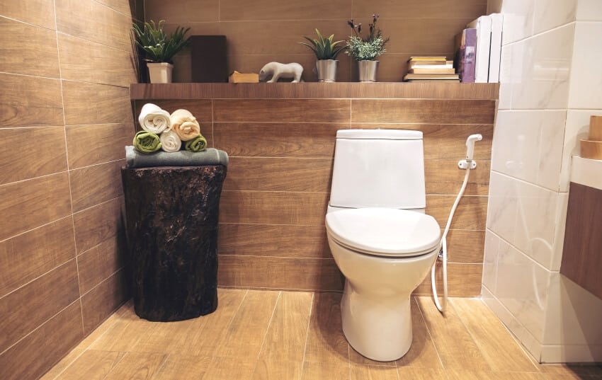 Современная ванная комната со стеной и полом из деревянной плитки и встроенной полкой с книгами, растениями и декором.