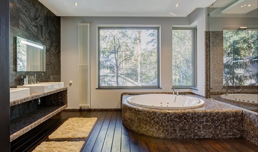 Современная ванная комната с туалетным столиком, деревянным полом и встроенной ванной с мозаичной плиткой.