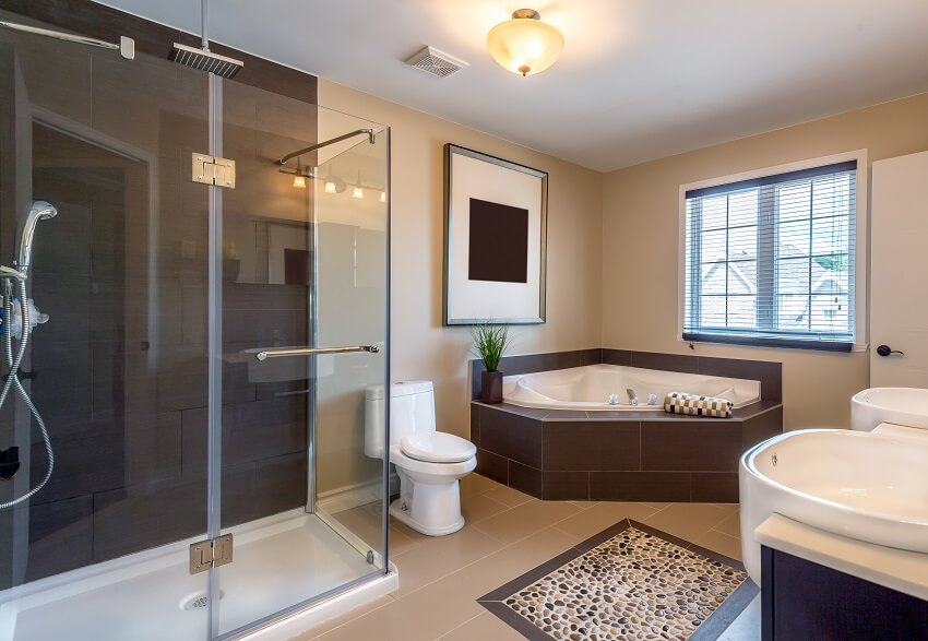 Бежевая теплая ванная комната с акцентным каменным полом, душевой кабиной, угловой ванной и двойной раковиной.