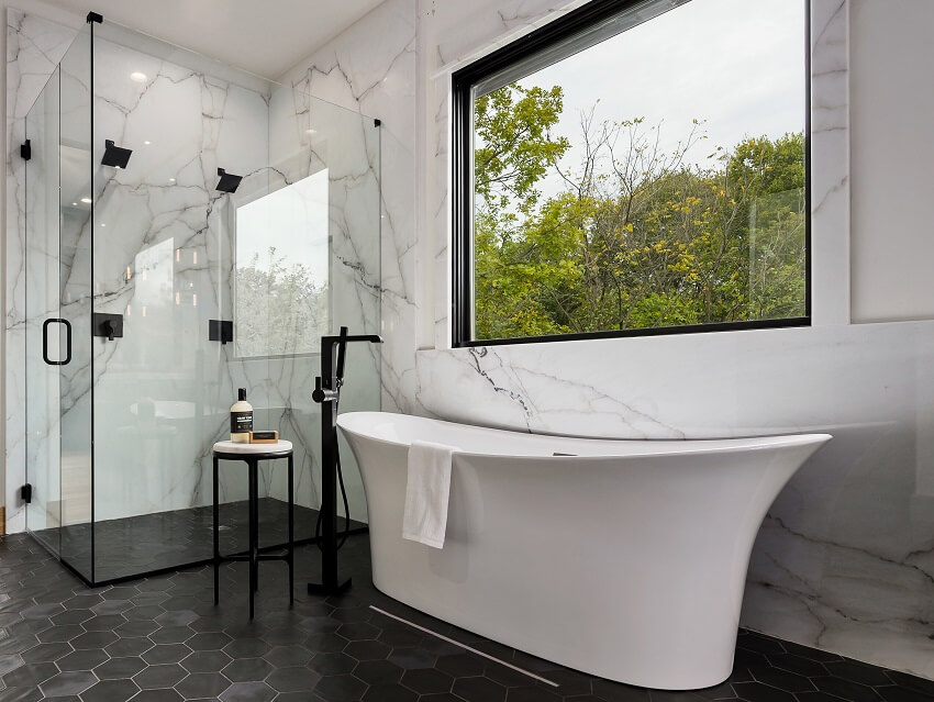 Современная ванная комната с полом из черной плитки, мраморной стеной, душем и отдельно стоящей ванной.