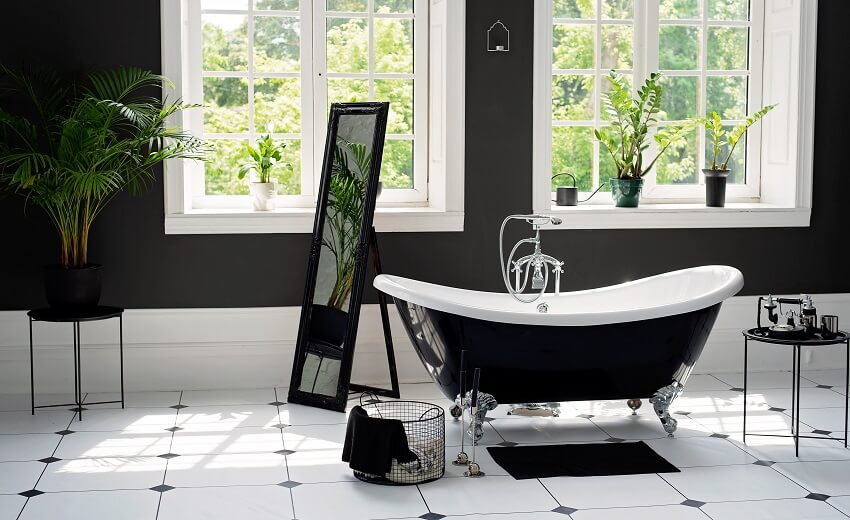Черно-белая ванная комната с большими солнечными окнами, растениями и ванной на ножках