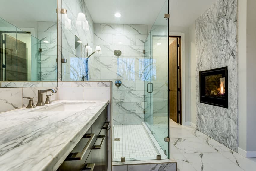 Bathroom with glass shower enclosure, Carrara marble tiles, countertop, floors, mirror, faucet, and fireplace