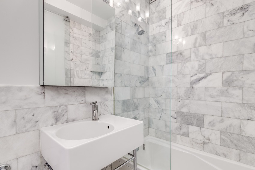 Bathroom with vanity mirror, Carrara marble shower, sink faucet, and tub