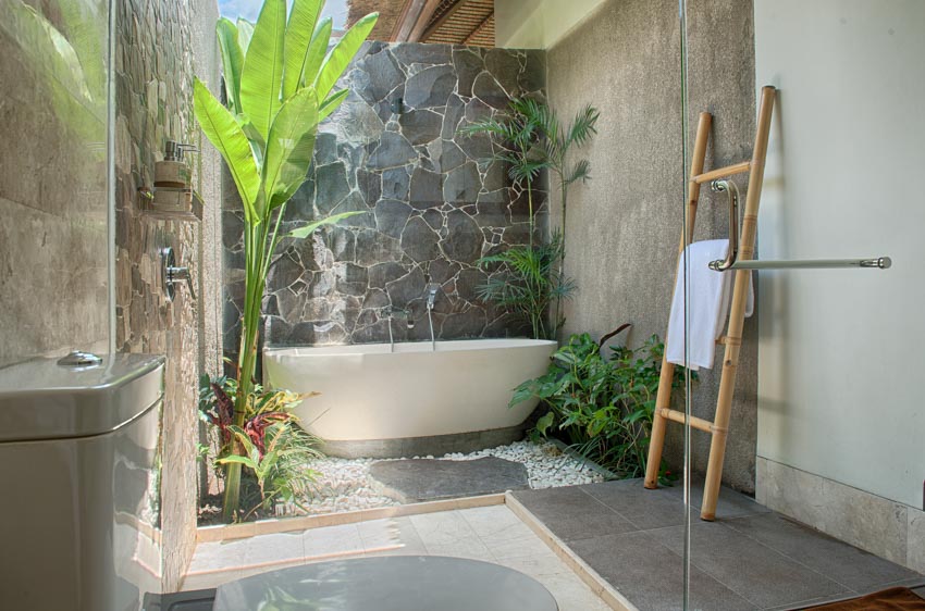 Luxurious outdoor bath with tub, stone wall, and plants