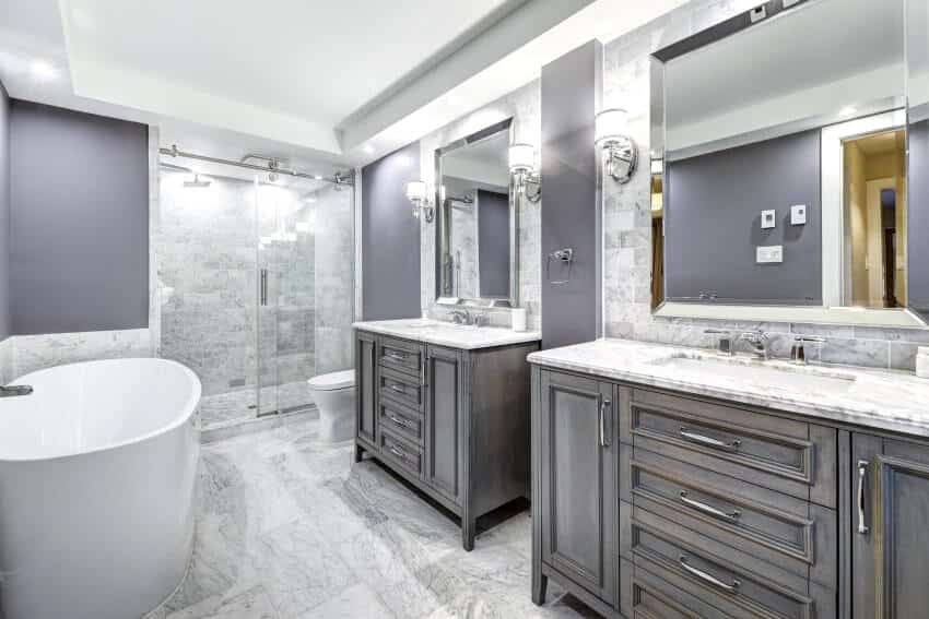 Серая ванная комната с отдельно стоящей ванной, настенными светильниками и мраморными столешницами, стенами и полом