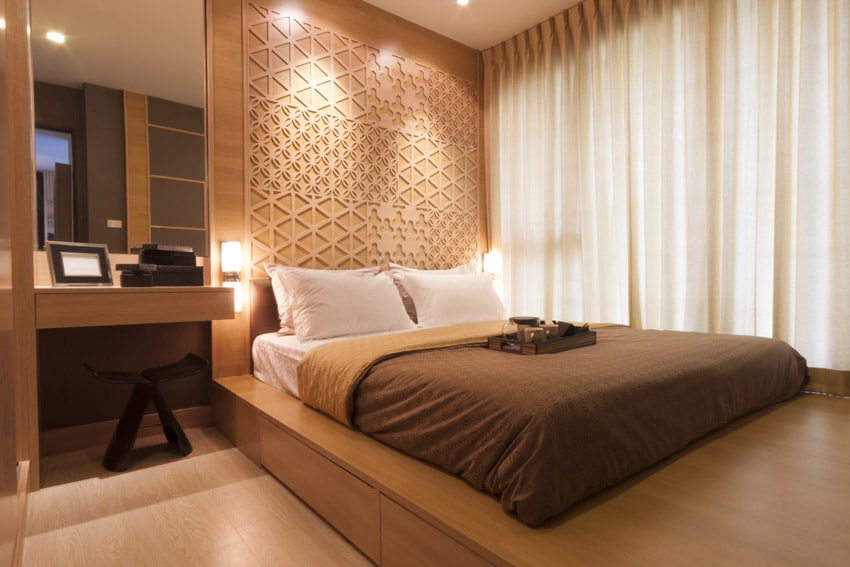 Спальня с теплым освещением, шторами, матрасом, подушками, акцентной стеной, табуретом, косметическим зеркалом и настенными бра.