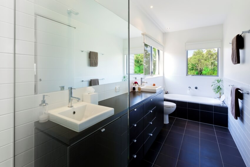 Современная ванная комната с черным кафельным полом, белыми стенами и окрашенными столешницами.