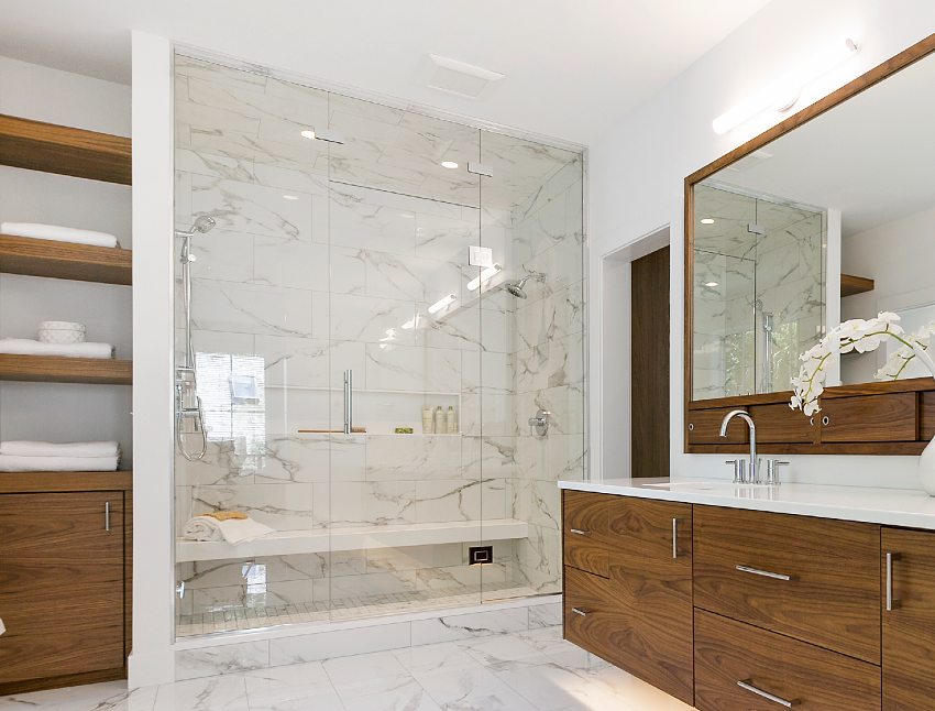 Потрясающий интерьер ванной комнаты с большим зеркалом над деревянными шкафами, мраморными полами и потолочной плиткой для душа