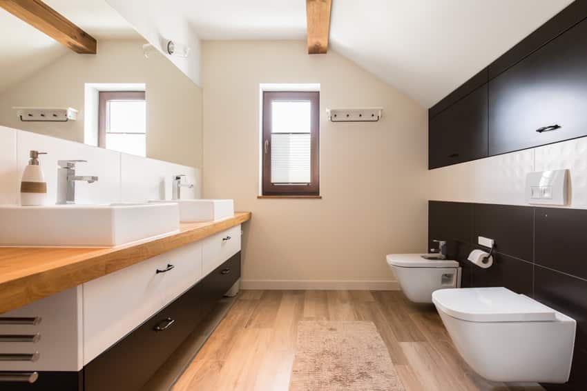 Bathroom with butcher block countertop, wood floor, window, toilet, bidet, mirror, and drawers