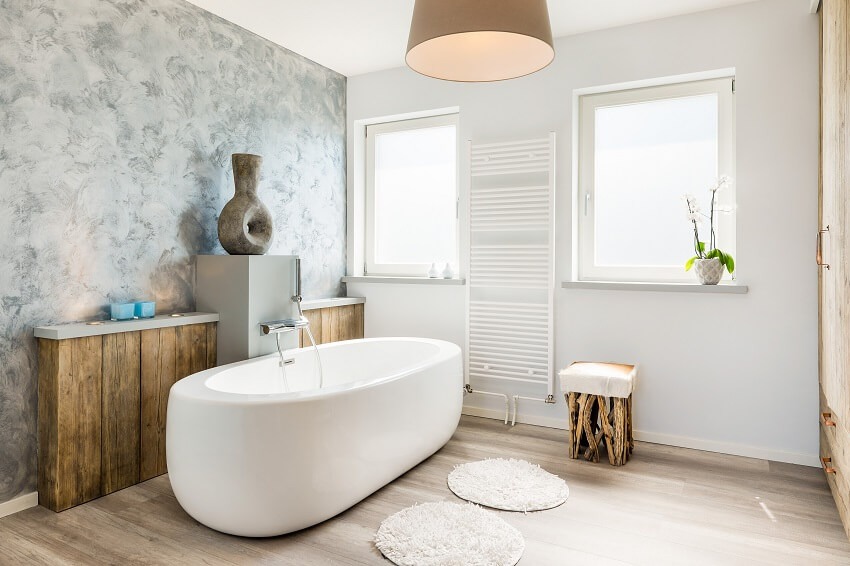 Modern bathroom with freestanding type of bathtub, round rugs, and wood stool