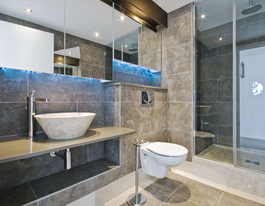 Bathroom with limestone wall tiles, flooring, toilet, sinks, mirror, and shower area