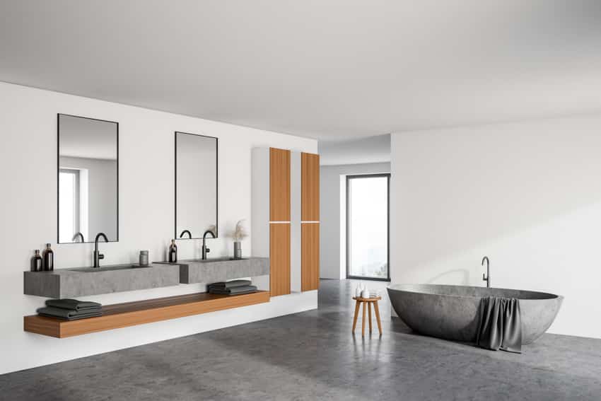 Минималистская ванная комната с ванной из натурального камня, бетонным полом, раковиной и зеркалами