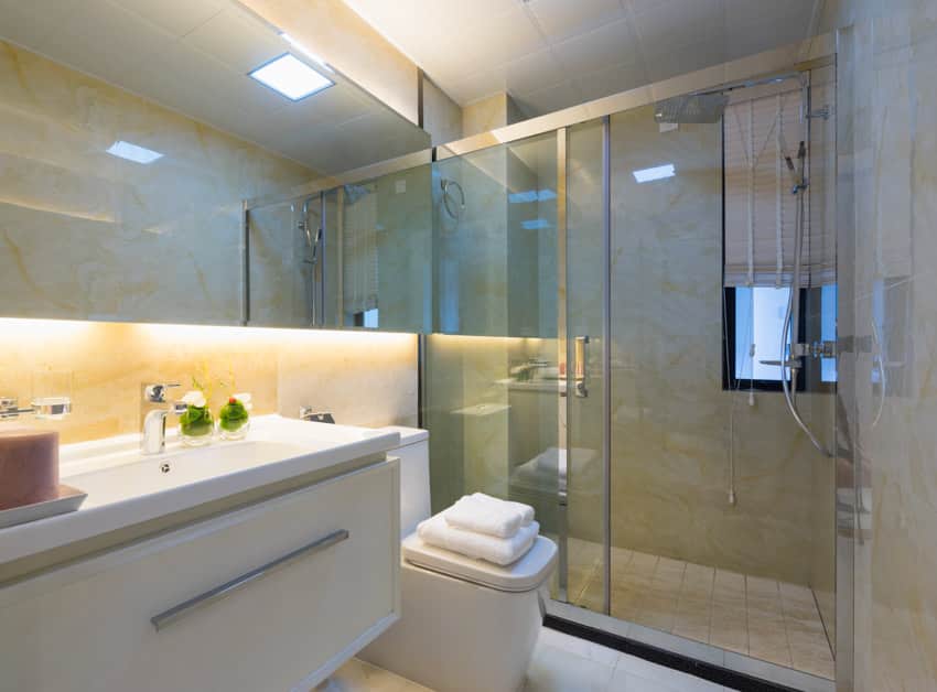 Ванная комната с эпоксидной стенкой для душа, стеклянной перегородкой, зеркалом, унитазом и раковиной.