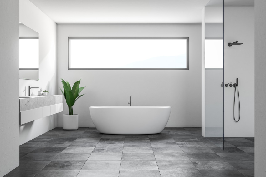 Ванная комната с серым плиточным полом, ванной, зеркалом, душевой, раковиной и комнатным растением.