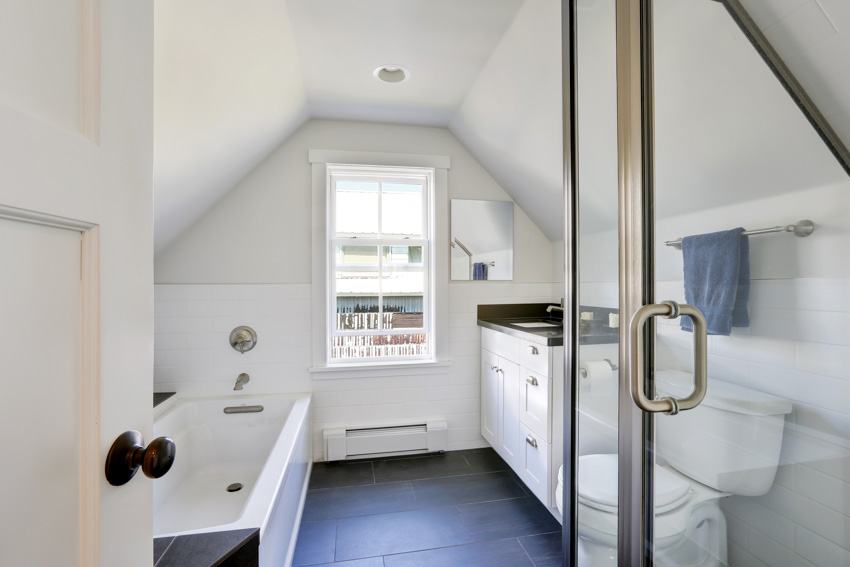 Ванная комната со сводчатым потолком, полом из сланцевой плитки, ванной, туалетом, раковиной и окном.