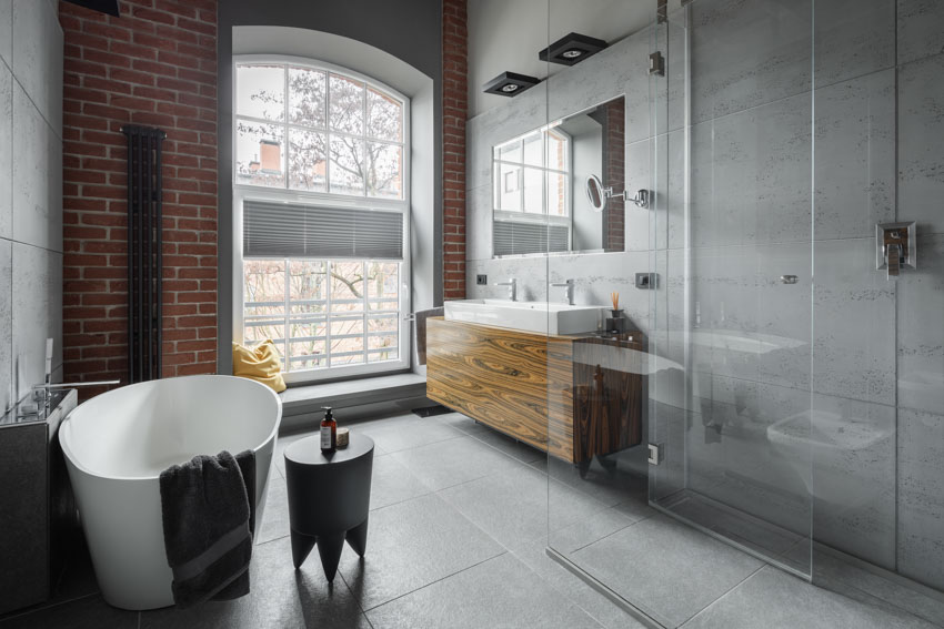 Ванная комната с сланцевым полом, ванной, раковиной, зеркалом, акцентной кирпичной стеной и окном.
